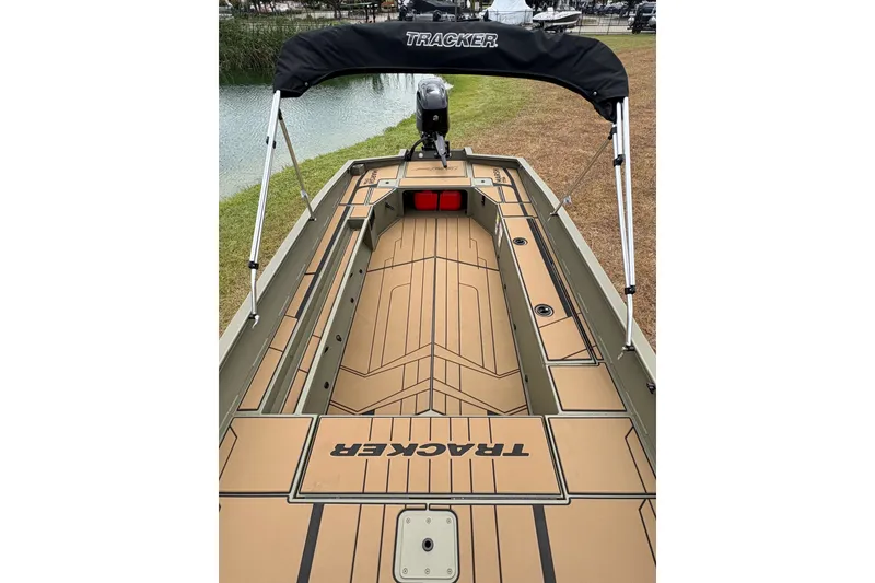 Slide: The Image of 2027 Tracker Grizzly 1756 T Marsh boat with canopy, docked by a grassy shoreline. - 21