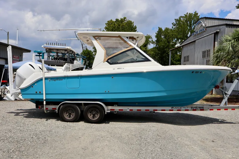 Slide: The Image of 2023 Edgewater 262CX Crossover boat on trailer, vibrant blue hull, parked outdoors. - 16