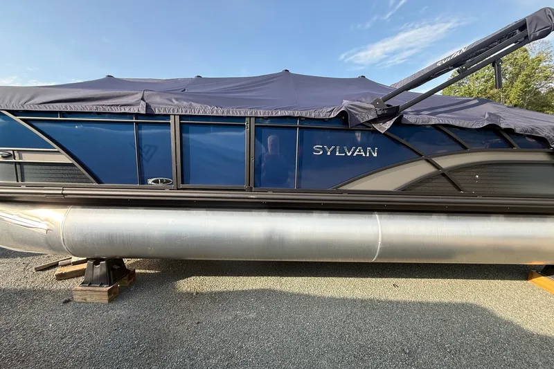 The Image of 2026 Sylvan L3 ULZ DH pontoon boat with cover, parked on gravel. - 1