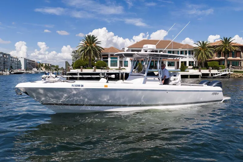 Slide: The Image of 2021 Intrepid 327 Nomad boat cruising near waterfront homes under a clear blue sky. - 1