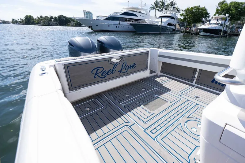 Slide: The Image of 2021 Intrepid 327 Nomad boat deck with "Reel Love" inscription, docked near luxury yachts. - 16