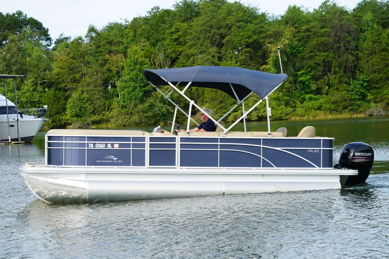 Slide: The Image of 2018 Bennington 22 SSX pontoon boat cruising on a lake with lush green trees. - 5