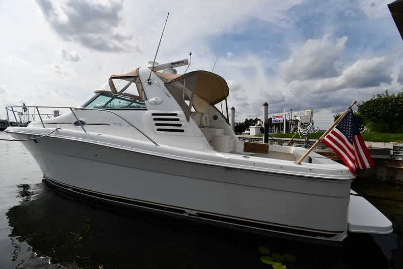 The Image of 2000 Sea Ray 330 Express Cruiser docked with American flag, under cloudy sky. - 1