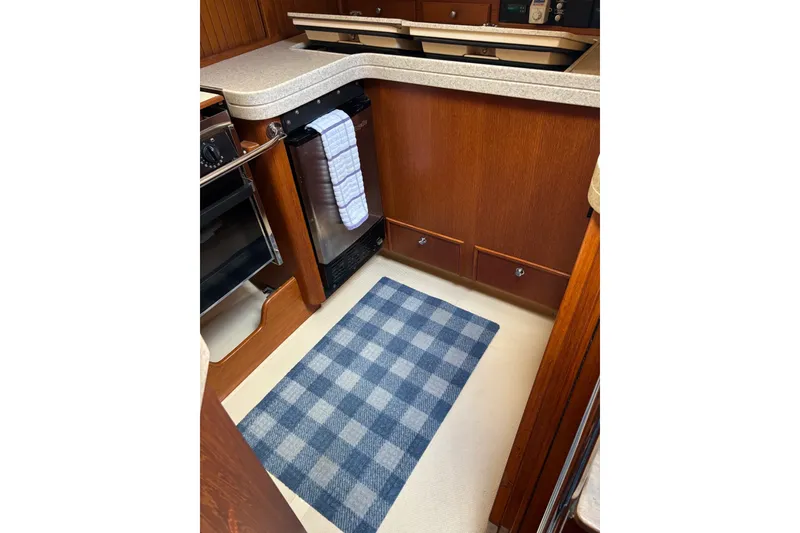 Slide: The Image of Island Packet 440 yacht kitchen interior, 2006 model, featuring wooden cabinetry and checkered rug. - 26