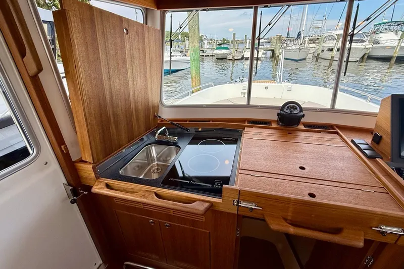 Slide: The Image of 2027 Targa 32 boat interior with wooden kitchenette, sink, and stove, overlooking marina. - 34