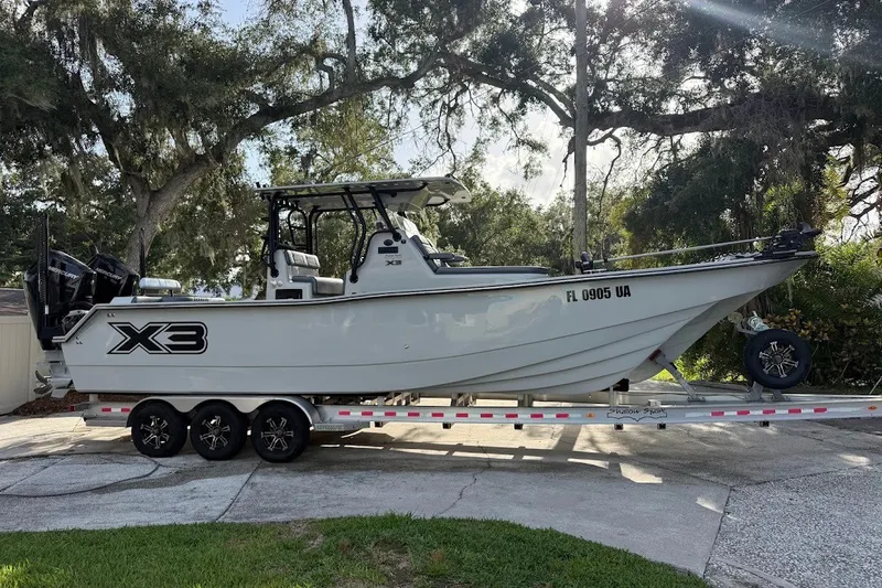 The Image of 2025 Shallow Sport 32 X3 boat on trailer, parked outdoors under trees. - 1