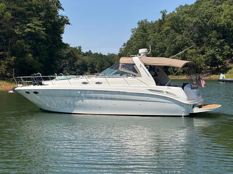 The Image of A white 1999 Sea Ray 380 Sundancer boat floats on a calm lake, surrounded by trees. - 0
