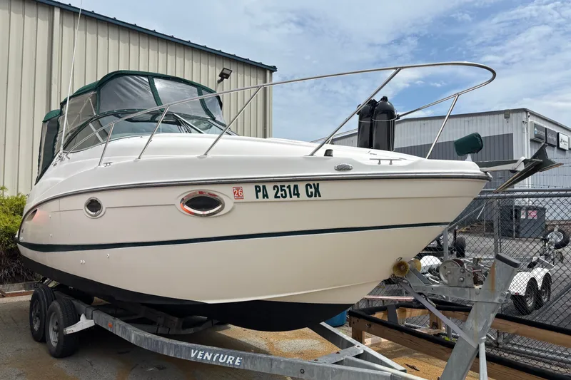 The Image of 2003 Maxum 2500 SCR boat on trailer, parked near industrial buildings. - 0