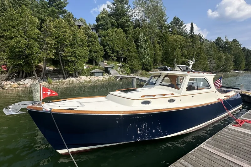 The Image of 2005 Hinckley Picnic Boat 36 EP docked by a scenic lakeside with lush greenery. - 0