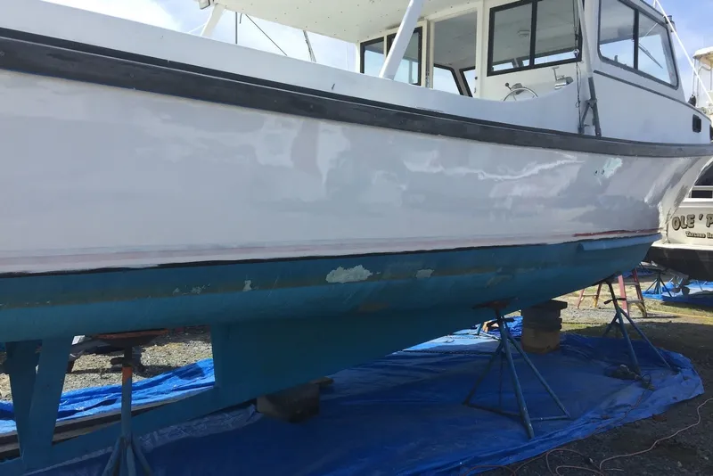 The Image of 1966 Uniflite Sportfisherman boat on stands, undergoing maintenance on a blue tarp. - 0