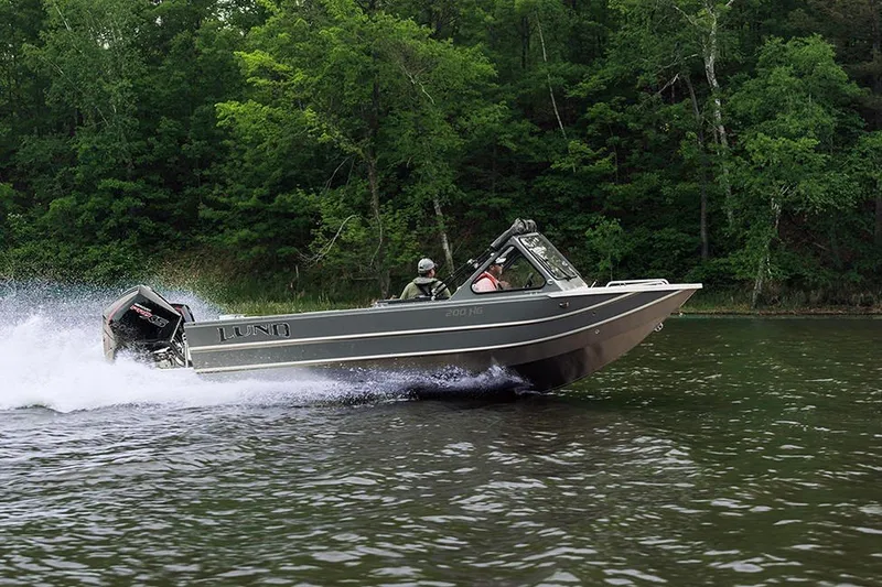 The Image of 2026 Lund 200 Heavy Gauge boat speeding on a lake with lush green forest backdrop. - 0