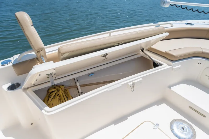 Slide: The Image of 2019 Scout 251 XSS boat with open storage compartment, beige seating, and ocean backdrop. - 26