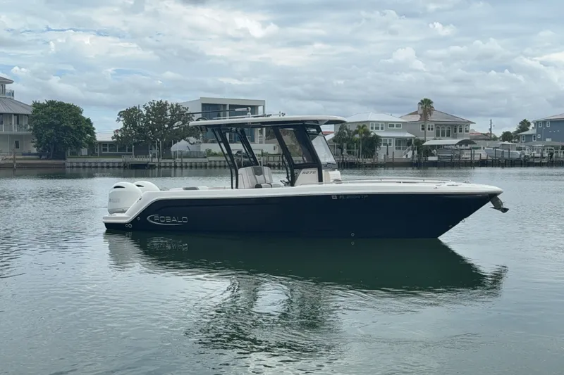 Slide: The Image of 2019 Robalo R272 Center Console boat on calm water, with waterfront homes in the background. - 30