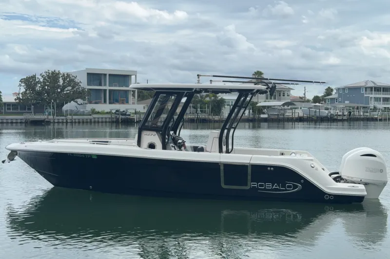 Slide: The Image of 2019 Robalo R272 Center Console boat on calm water, with modern waterfront homes in the background. - 28