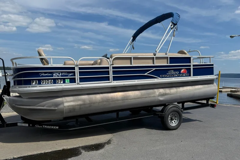 The Image of 2016 Sun Tracker Fishin' Barge 20 DLX pontoon boat on trailer by a lake. - 1