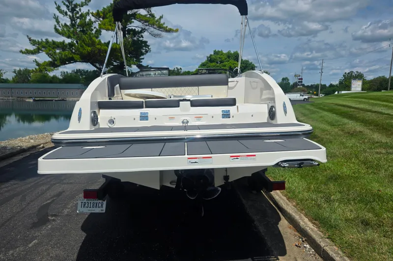 Slide: The Image of 2020 Bayliner DX 2250 boat rear view with swim platform, parked near a grassy area. - 2