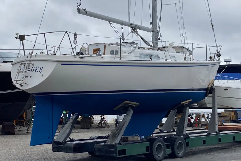 Slide: The Image of 1976 Pearson 10M sailboat on trailer, white hull with blue accents, docked outdoors. - 38