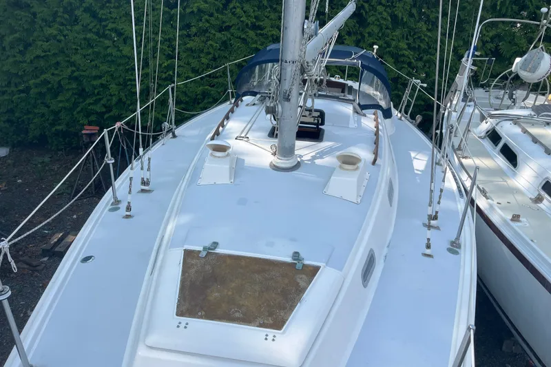 Slide: The Image of 1976 Pearson 10M sailboat deck with mast and rigging, surrounded by greenery. - 16