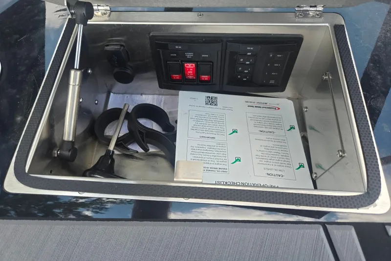 Slide: The Image of Control panel inside a 2025 Centurion Nv233 boat compartment with switches and documents. - 28