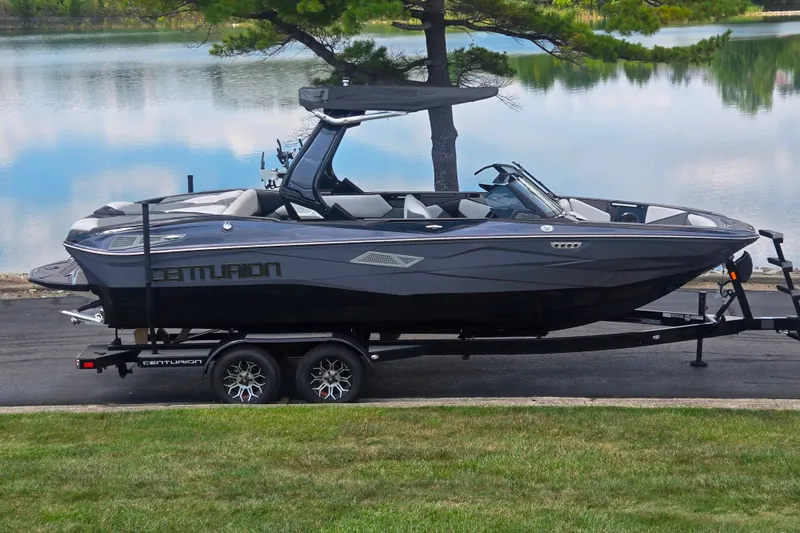 The Image of 2025 Centurion Nv233 boat on trailer by a serene lake. - 0