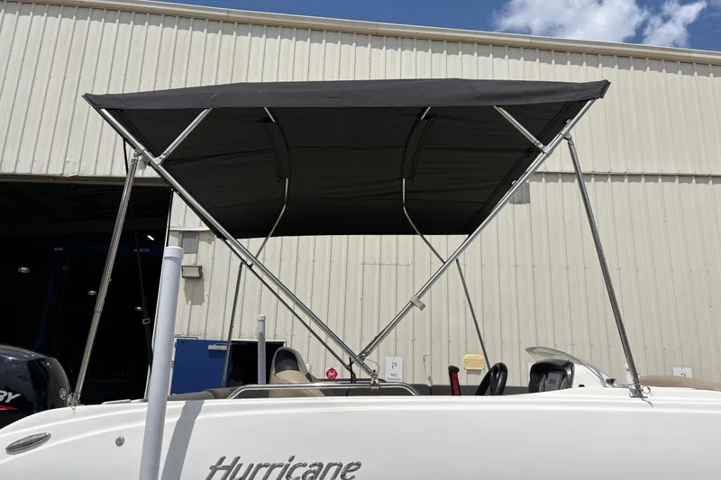 Slide: The Image of 2022 Hurricane SunDeck Sport 201 OB boat with black canopy, parked near a warehouse. - 16