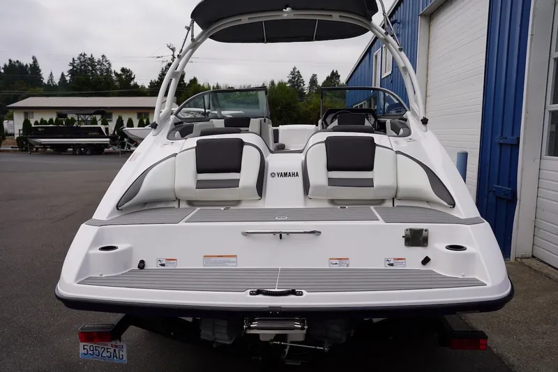 Slide: The Image of 2022 Yamaha Boats AR210, rear view, white exterior, parked near blue building. - 7