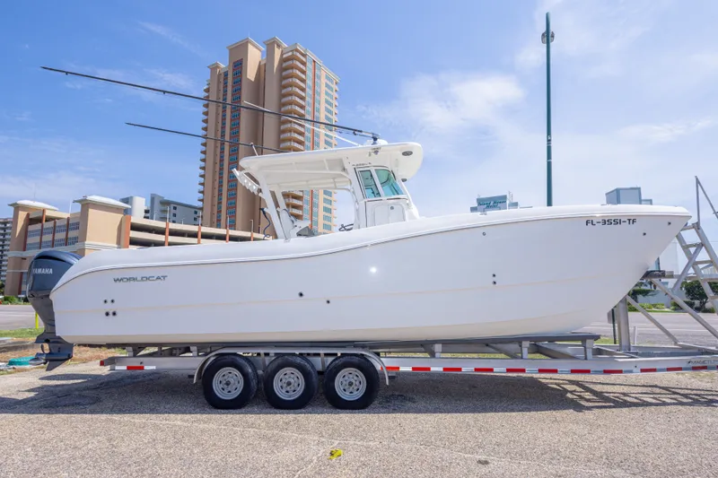 Slide: The Image of 2022 World Cat 325 CC boat on trailer, parked near tall buildings under clear sky. - 12