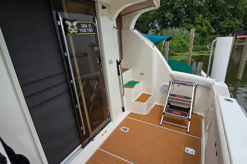 Slide: The Image of 2001 Silverton 330 Sport Bridge boat deck with steps and ladder, docked by lush greenery. - 4