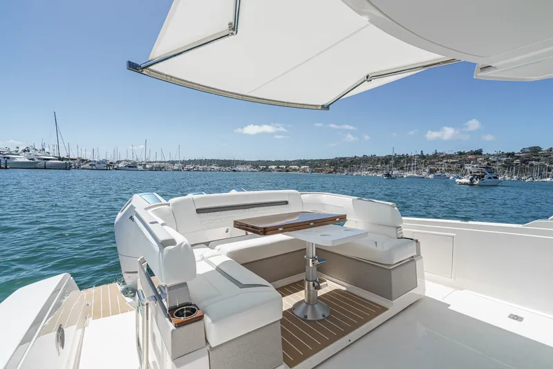 Slide: The Image of The image shows the stern of a 2024 Tiara Yachts 38 LS with elegant seating and a table under a sunshade, set against a scenic harbor. - 29