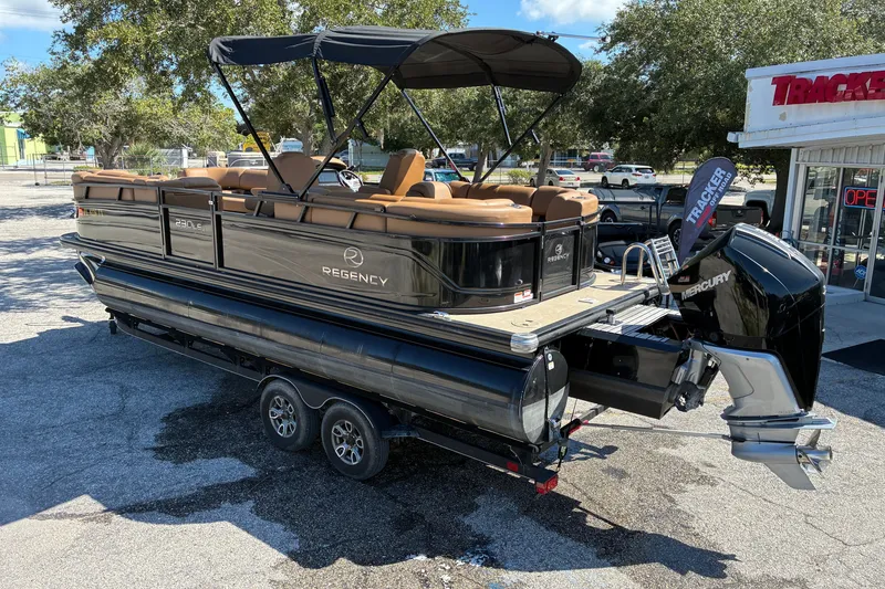 Slide: The Image of 2024 Regency 230 LE3 pontoon boat with Mercury engine on trailer, parked outdoors. - 2