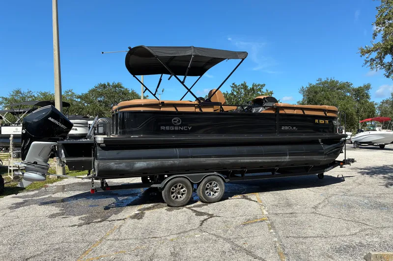 Slide: The Image of 2024 Regency 230 LE3 pontoon boat on trailer, parked outdoors under clear sky. - 3