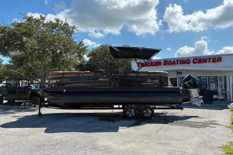 Slide: The Image of 2024 Regency 230 LE3 pontoon boat at Tracker Boating Center, under a clear blue sky. - 1