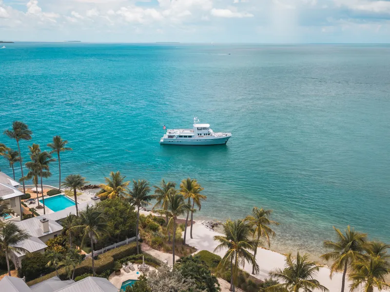 Slide: The Image of A luxury yacht is anchored off a tropical coast with palm trees and clear water. - 18