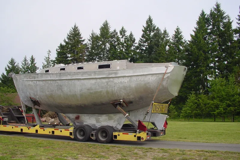 Slide: The Image of Large Brewer Cutter boat from 2005 on a trailer, surrounded by trees. - 68