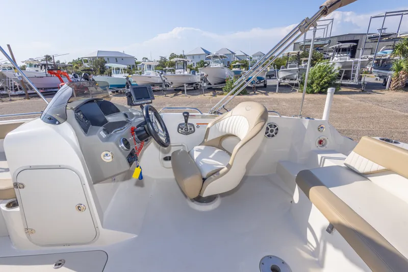 Slide: The Image of 2018 Stingray 192 SC boat interior with steering wheel and seating, docked outdoors. - 22
