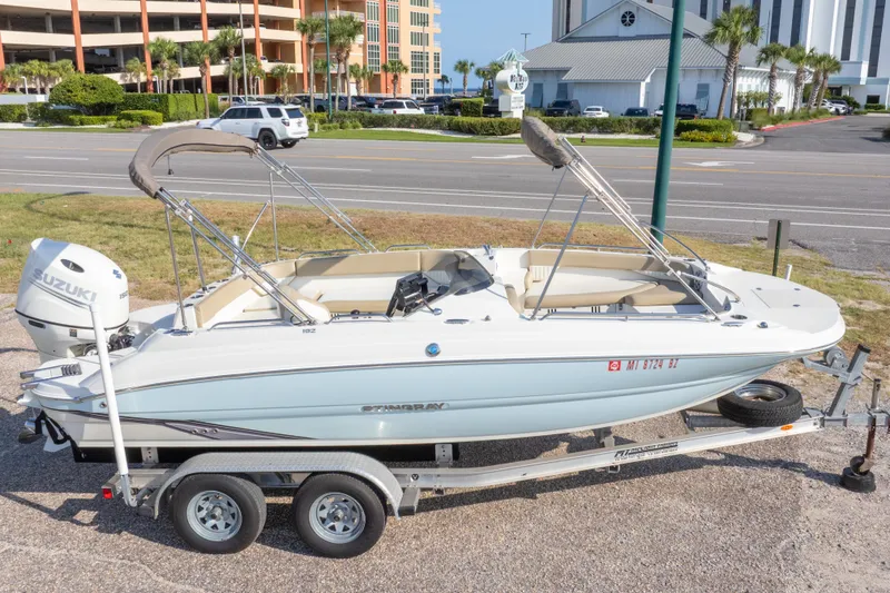 Slide: The Image of 2018 Stingray 192 SC boat on trailer with Suzuki outboard motor, parked roadside. - 1