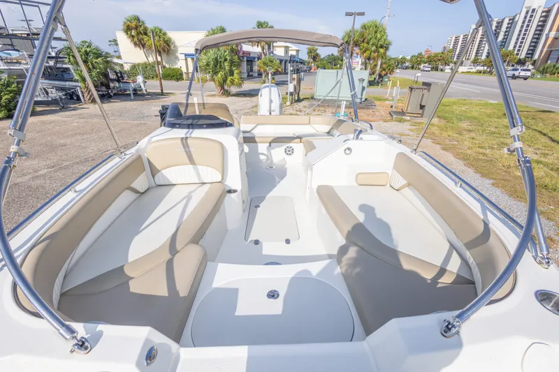 Slide: The Image of 2018 Stingray 192 SC boat interior with beige seating and canopy, parked outdoors. - 28