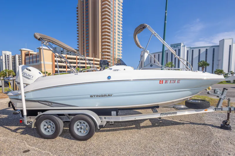 Slide: The Image of 2018 Stingray 192 SC boat on trailer, parked near tall buildings under clear blue sky. - 12