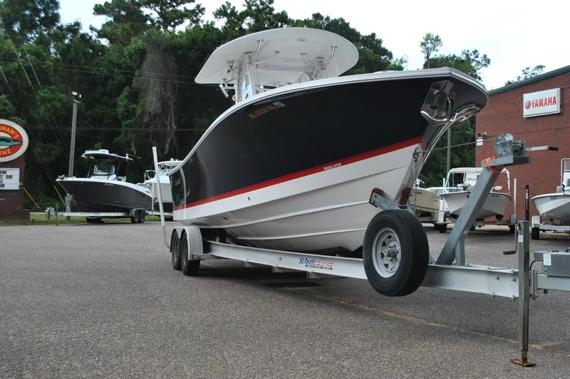 Slide: The Image of 2016 Regulator 28 Forward Seating boat on trailer at dealership, surrounded by trees and signage. - 5