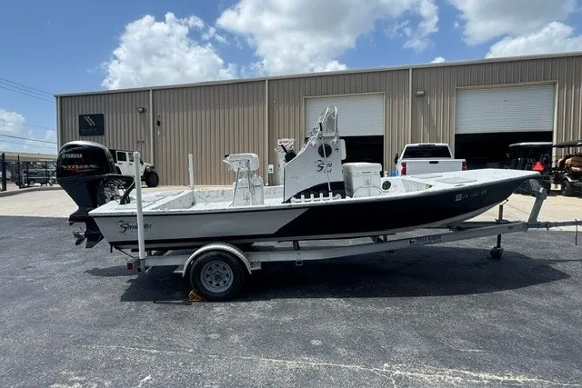 The Image of 2018 Shoalwater 20' Catamaran on trailer, parked outside industrial building under blue sky. - 0