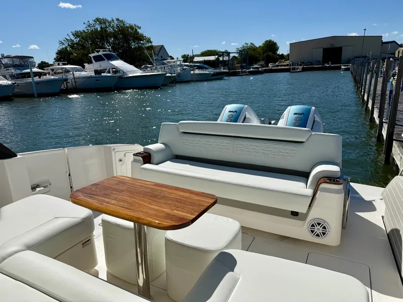 Slide: The Image of The image shows the stern of a 2027 Tiara Yachts 39LS. There's a bench seat and a wooden table. Boats are visible in the harbor background. - 6