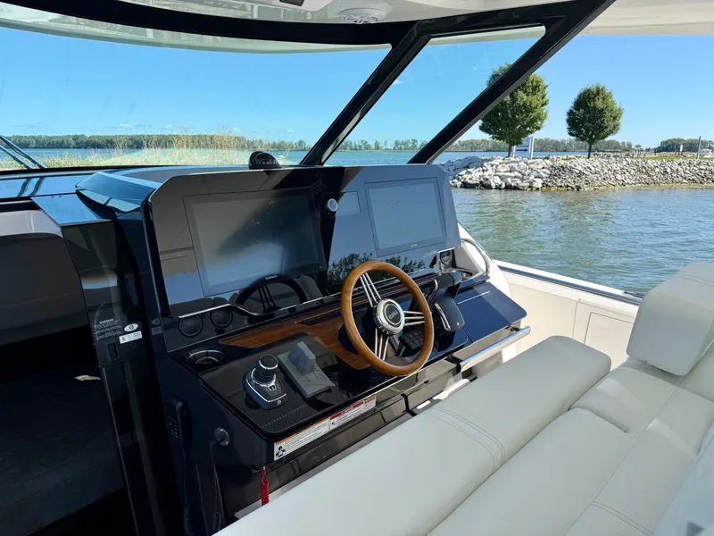 Slide: The Image of The image shows the cockpit of a 2027 Tiara Yachts 39LS. It features a modern steering wheel and large screens, with a view of water and trees in the background. - 15