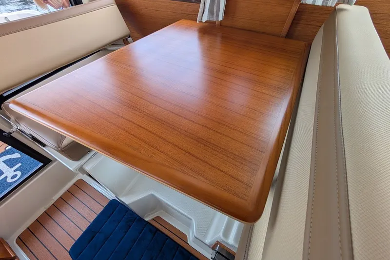 Slide: The Image of 2023 Ranger Tugs interior with polished wooden table and beige seating. - 17