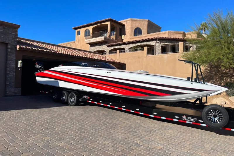 Slide: The Image of 2023 Daves Custom Boats M37R with red stripes on a trailer in front of a luxury home. - 0