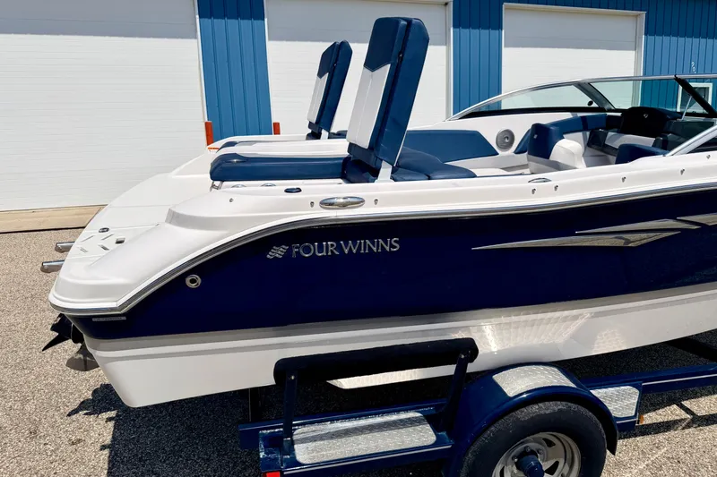 Slide: The Image of 2014 Four Winns H200 boat on trailer, blue and white exterior, parked near blue building. - 8
