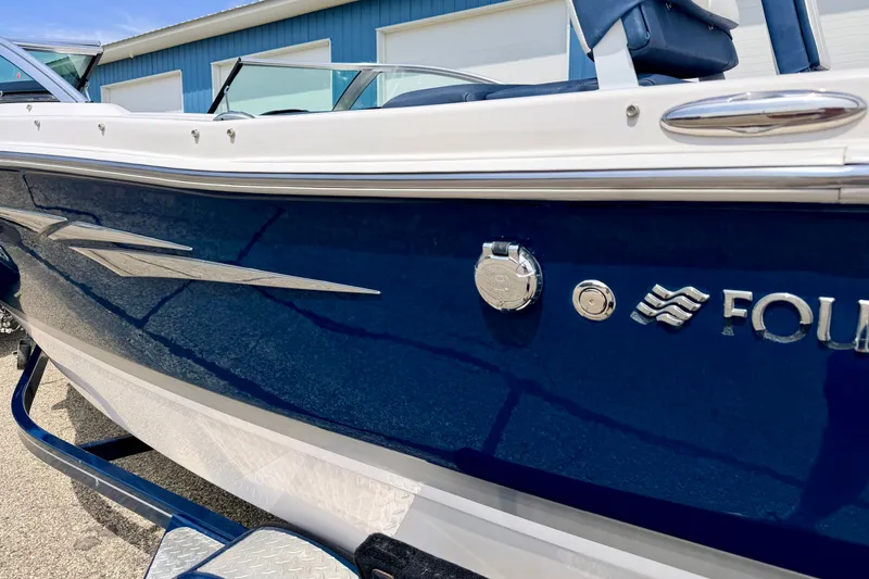 Slide: The Image of 2014 Four Winns H200 boat, blue and white exterior, parked near a building. - 13