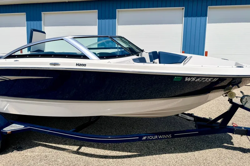 Slide: The Image of 2014 Four Winns H200 boat on trailer, parked outside blue building. - 9