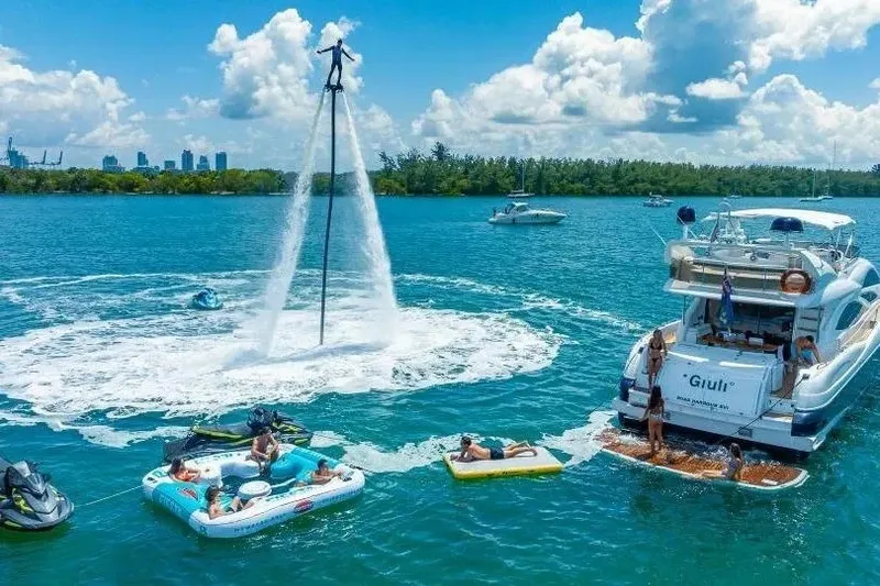 Slide: The Image of Sunseeker Manhattan 74 yacht with people enjoying water activities and flyboarding in a scenic bay. - 15