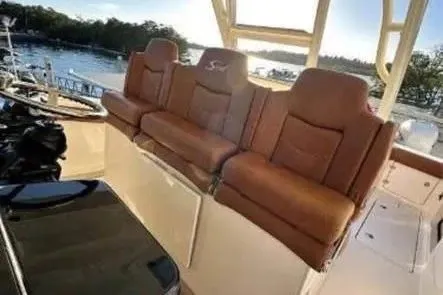 Slide: The Image of 2019 Scout 420 LXF boat with brown leather seating, docked by a scenic waterfront. - 15