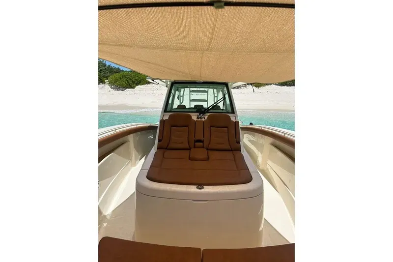 Slide: The Image of 2019 Scout 420 LXF boat interior with brown seating, shaded canopy, and beach view. - 29